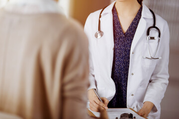 Doctor and patient discussing current health examination while sitting in sunny clinic. Perfect...