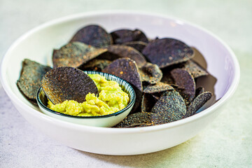 Black potato chips with avocado dip - guacamole, white background. Vegan food concept.