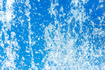 Jets of water with a lot of drops and bubbles under the rays of the sun on a blue background. A large plan The texture of the water waves of a large fountain