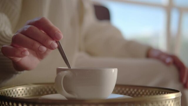 Time for coffee: woman in a white sweater is stirring sugar in a cup