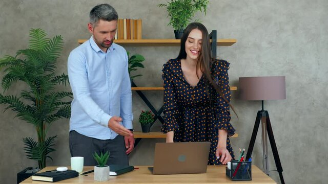 Smiling woman and man greet elbows employees work together in office preparing presentation for meeting. Manager showing progress report to businessman on laptop computer. 4K slow motion footage