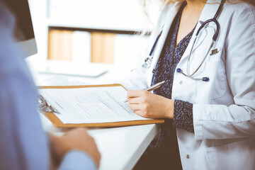 Female doctor and male patient discussing current health examination while sitting in clinic,...
