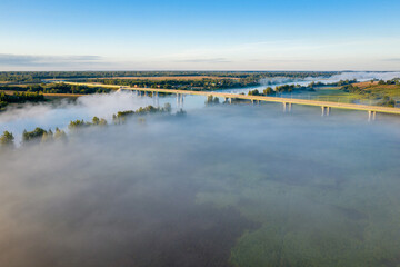 Early morning landscape. Foggy river. Highway bridge across the Volkhov river. River valley in the morning fog at sunrise. View from above. Rays of the sun breaking through the fog in over the trees