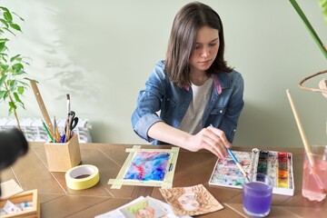 Teenager girl painting with watercolors, sitting at home at the table