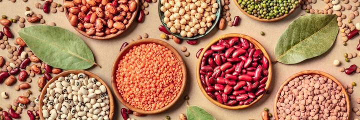 Legumes assortment, overhead panorama on a brown rustic background. Lentils, soybeans, chickpeas,...