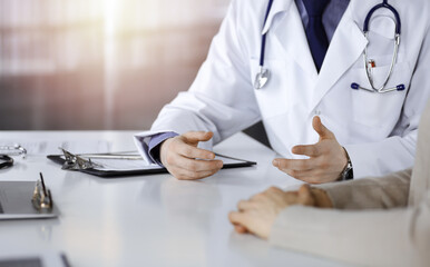 Unknown male doctor and patient woman discussing something while sittingin a darkened clinic, glare...