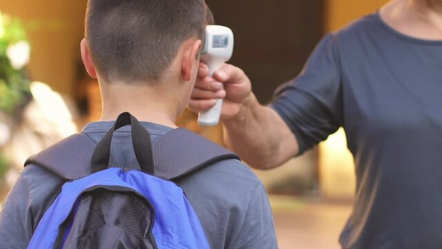 Teacher checking the temperature to a schoolboy before cpming into the school. Covid-19 Coronavirus prevention. Education, lifestyle. Slow motion.