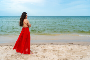 Fototapeta na wymiar happy woman in red dress standing with arms crossed on sea beach