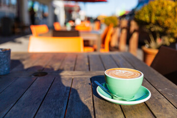 Hot cafe latte with latte art in green cup on wooden table in Hokitika, New Zealand.