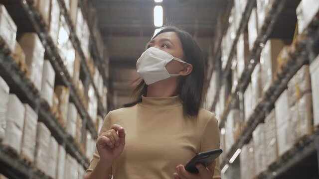 Asian woman wearing mask walking in warehouse and use smart phone for check price.