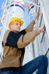 young manual worker climbing enclosed metal ladder