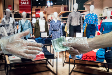 the buyer in plastic gloves gives the buyer dollars for the goods in the clothing store. coronavirus