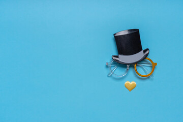 Photo booth props cylinder hat, glasses and nose of heart shape on blue background. Greeting card for father's day. Creative composition in minimal style, flat lay
