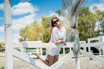 Fototapeta na wymiar Pretty girl enjoy nature at sunny day in white wooden gazebo near the lake