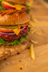 Big tasty homemade burger with bacon, lettuce, tomato, cheese, ketchup and mustard on the wooden board with some french fries isolated on light beige background, Fast food concept.