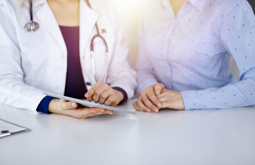 Unknown woman-doctor is showing to her patient a description of medication, while sitting together...