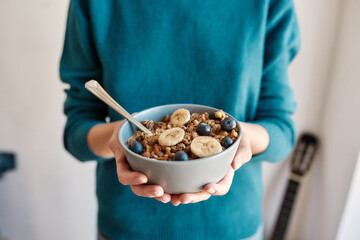 Close up of hands of woman holding homemade granola in a plate with nuts, honey, blueberries, banana and other natural ingredients, Focus on a bowl