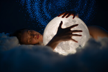 Young attractive girl sleeping on the soft cloud and hugs the bright white moon. Girl with the moon...