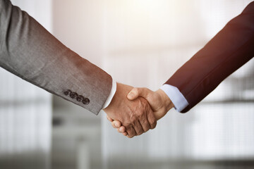 Business people standing and shaking hands in sunny office, close-up. Handshake and marketing