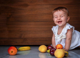 Fototapeta premium happy cute baby crawling on the floor with fruits apples, plums, bananas, mango on the wooden background