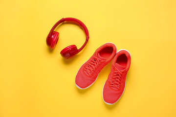 Sportive shoes and headphones on color background