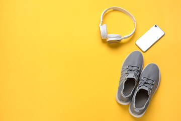 Sportive shoes, mobile phone and headphones on color background