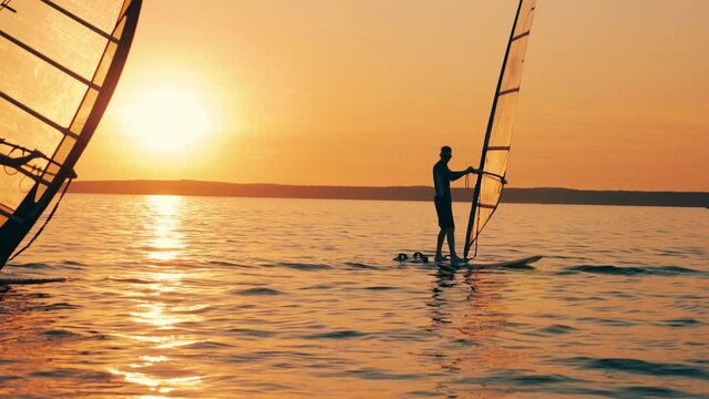 Two men are sailing on windsurf boards at sundown