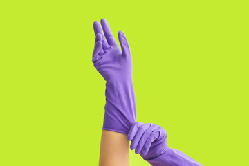 Woman putting on rubber gloves against color background