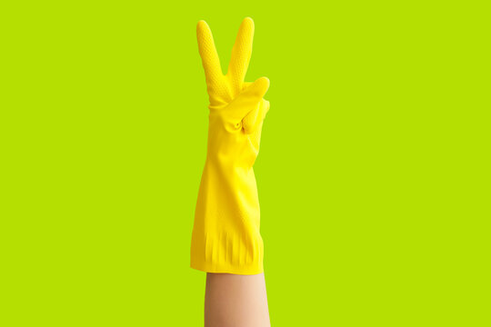 Hand in rubber glove showing victory gesture on color background
