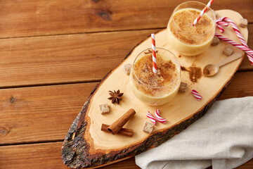 christmas and seasonal drinks concept - glasses with eggnog, ingredients and aromatic spices on cut wood board