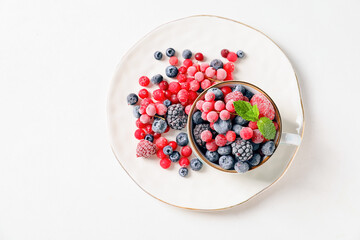 Cup and plate with tasty frozen berries on white background