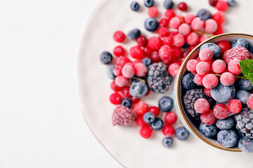 Cup and plate with tasty frozen berries on white background