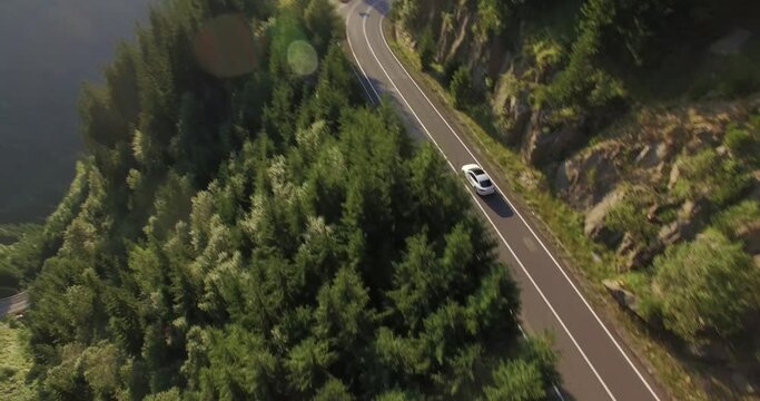 White sedan driving along the Transfagarasan Highway in the Carpathian mountains in Europe. Dramatic landscape captured by aerial drone
