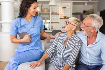 Obraz premium Portrait of female nurse with senior patients siting on sofa while being in a home visit.