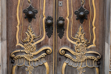 Beautiful old door knocker, carved architectural elements, door handles, brown and gold colors. Close-up photo.