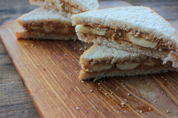 Close-up of Peanut butter banana sandwiches on wooden background. Slices of whole wheat bran bread with peanut paste on a cutting board. Healthy snack for kids.	