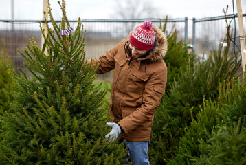 winter holidays, sale and people concept - happy smiling man choosing or selling christmas tree at...