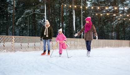 christmas, family and leisure concept - happy mother, father and daughter with support frame at outdoor skating rink in winter