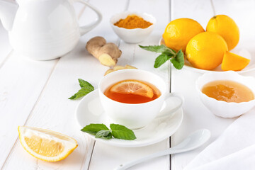 Antioxidant healthy tea with lemon, ginger, honey, turmeric and mint on a white wooden table. The concept of alternative medicine.
