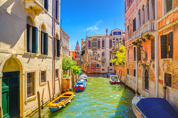 Venice cityscape with narrow water canal Rio de San Agostin with colorful boats moored between old buildings, Veneto Region, Northern Italy. Typical Venetian view, blue sky background in summer day