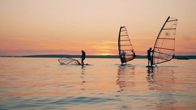 Group of men on sailboards with one of them falling