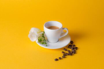 Cup of espresso on yellow background with flower.