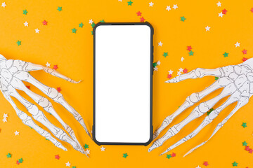Smartphone is surrounded by skeleton hands made of paper. Orange background with decorative stars....