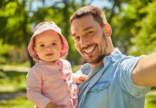 family, fatherhood and people concept - happy father taking selfie with baby daughter at summer park