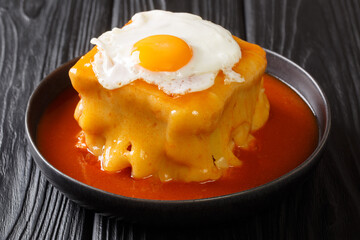 Portuguese delicious Francesinha sandwich with meat sausages, melted cheese, drizzled with tomato beer sauce and topped with a fried egg close-up in a plate on the table. horizontal