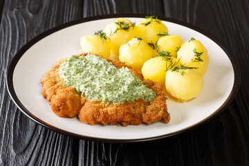 Portion of fried breaded schnitzel with boiled potatoes and Frankfurt green sauce close-up in a plate on the table. horizontal
