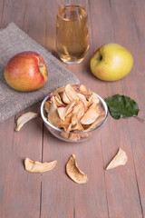 Apple chips in a glass plate, an Apple on a napkin, a glass of Apple juice on a colored wooden background. Vertical orientation