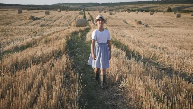 Pretty girl in blue dress walks in a field with haystacks.