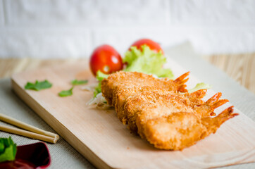 Butterfly ebi furai shrimp served with tomato and lettuce on a wooden chopping board along with ketchup