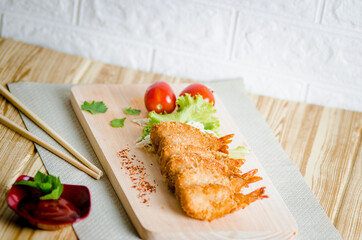 Butterfly ebi furai shrimp served with tomato and lettuce on a wooden chopping board along with ketchup